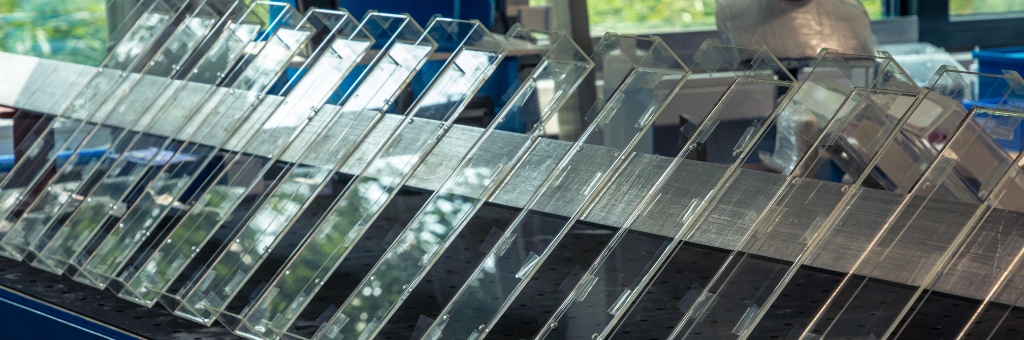 Een rij transparante plastic platen rechtop geplaatst op een metalen rek, met licht dat weerkaatst op hun oppervlakken in een werkplaatsomgeving.