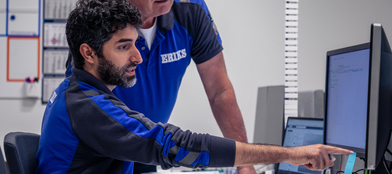 Twee ERIKS-medewerkers werken samen bij een computer, waarbij de een naar het scherm wijst en de ander toekijkt.
