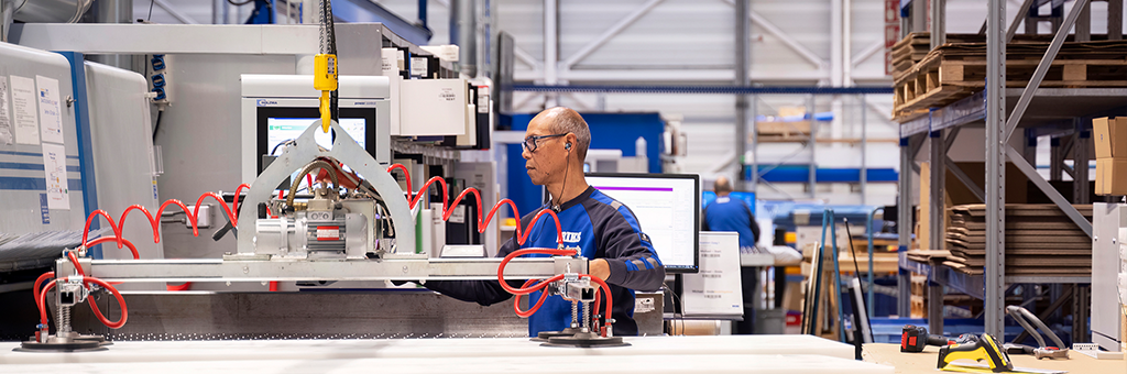 Een ERIKS-medewerker bedient een machine met zuignappen om grote plastic platen te tillen en te verplaatsen in een goed georganiseerde industriële werkruimte.